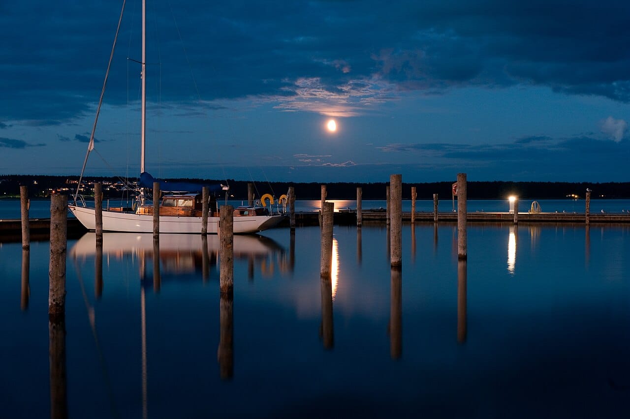 De haven van Mariehamn op Åland in het blauwe uur, met een afgemeerde zeilboot en de maan boven het water